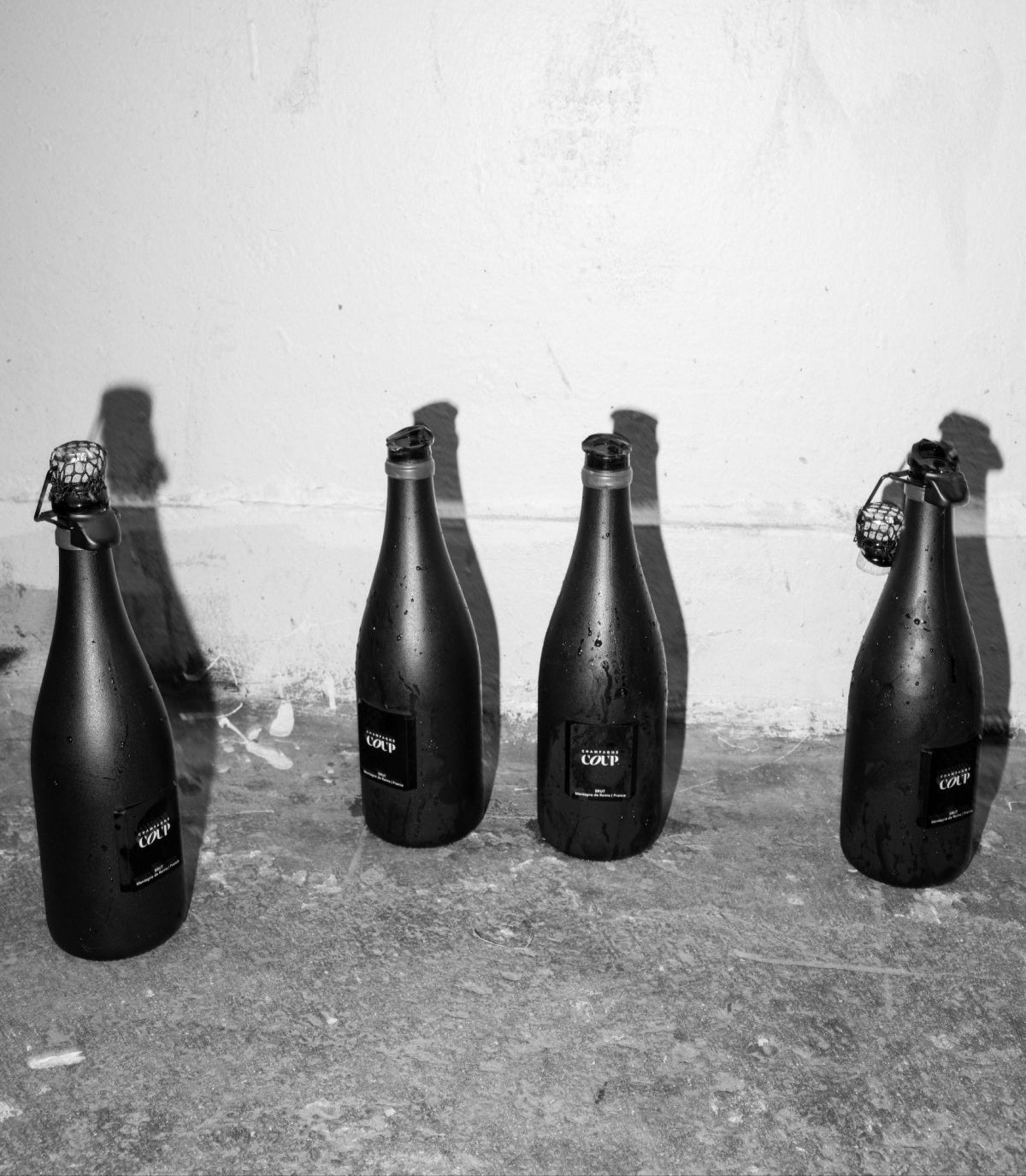 Four black bottles with 'COVP' labels on a concrete surface.